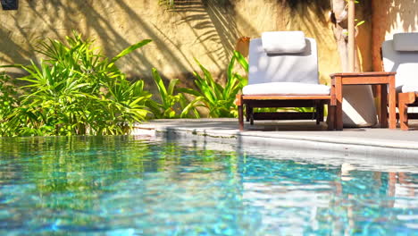 an empty sun lounger sits on the edge of a swimming pool waiting for its next adventure