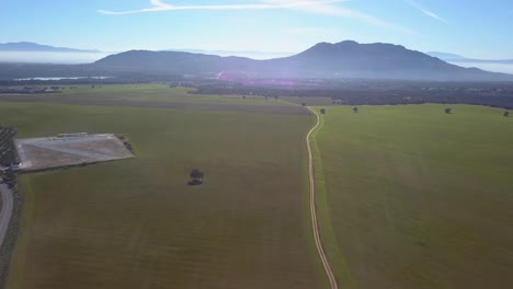 Aerial-view-of-an-extense-meadow-in-a-sunny-hazy-day-with-mountains-in-the-background