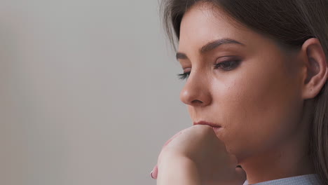 Unhappy-young-woman-touches-chin-by-hand-on-light-background