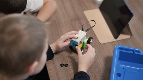 children intently focused on assembling parts from a robotics kit, with a tablet displaying instructions, promoting stem learning and creativity