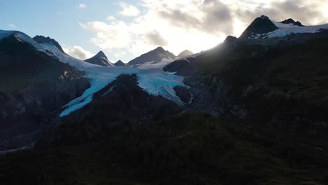 Silhouette-of-partially-snowcapped-Alaskan-mountains-against-the-bright-sun-in-summer