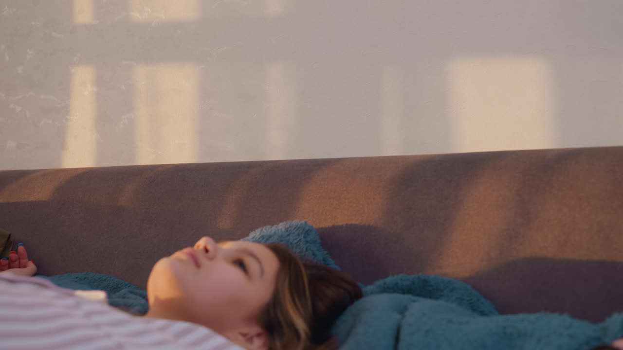Girl Looking Out Window Peacefully, Serene Young Lady Observing Sunlight Casting Shadows On Wall, Contemplative Young Woman In Striped Pajamas Gazes Toward Window With Tranquil Bedroom Ambiance