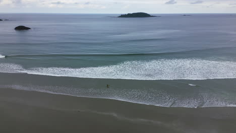 surfista solitario en la bahía de cox en tofino, bc - vista aérea del océano y la playa