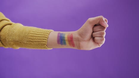 mano de un hombre biracial con bandera lgbt en el brazo sobre fondo púrpura