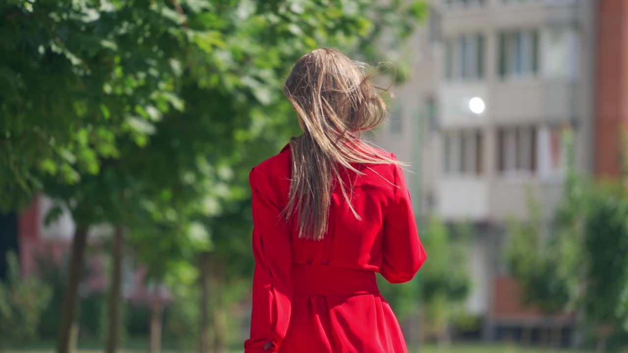 Slow motion of woman walking outdoors. Back view of a young female in red dress in the city. Long hair of attractive girl.