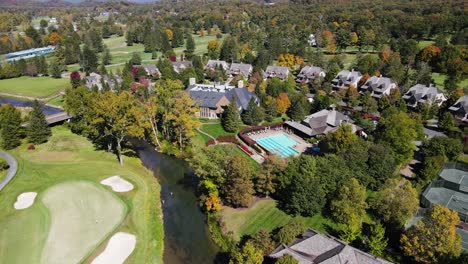 Aerial-wide-rotating-parallax-shot-of-private-clubhouse-and-pool-located-on-golf-course-with-houses-and-mountains-in-the-background-during-summer