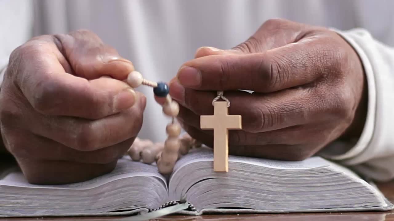 Mani che pregano Dio su una Bibbia con persone - Filmato video in stock
