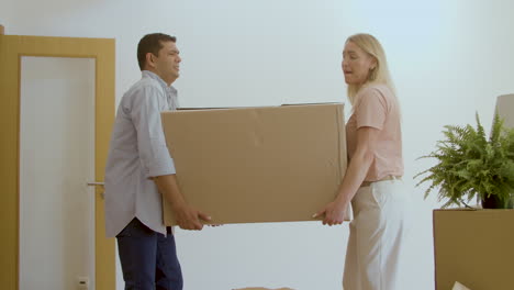 wife and husband carrying big box into new house together