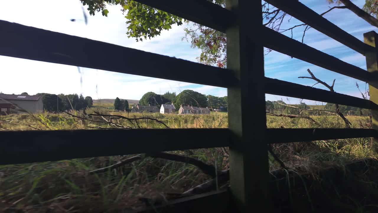 Quiet rural English scene with a weathered wooden fence, open fields, and distant cottages