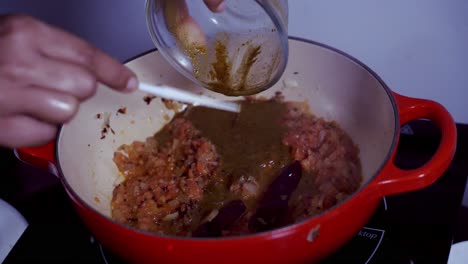 pouring a curry blend paste into a pot of crushed tomatoes to make a curry dish