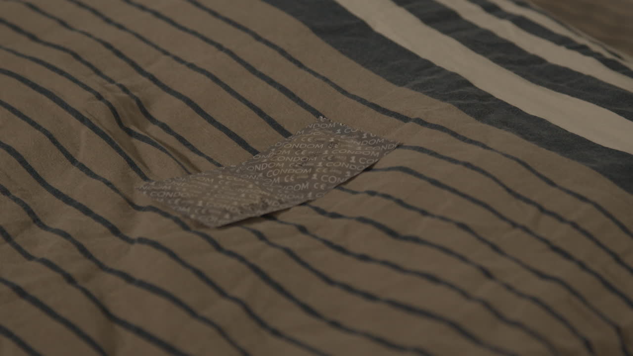 침대에 베개에 누워 래핑된 콘돔 쌍의 인형을 닫습니다.