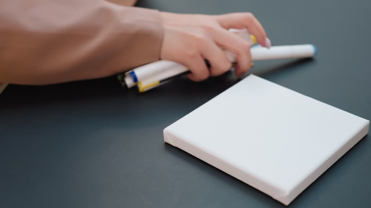 미술 용품으로 깨끗하게 정리된 작업 공간, 검은색 테이블 위에 손으로 펜을 정리하는 모습, 마커와 툴을 정리하는 백인 디자이너, 툴과 스케치로 깔끔하게 정돈된 아티스트 작업 공간 클로즈업