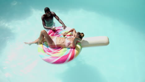 relaxing in pool, diverse couple enjoying summer on colorful inflatable float