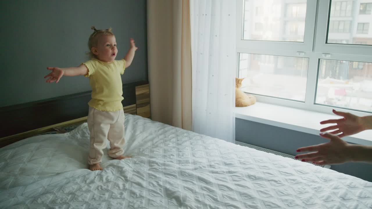 Menina pequena feliz em pé e brincando na cama.