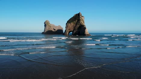 Wharariki-Beach,-stunning-archway-rock-formation-birds-eye-view-fly-over-the-sea