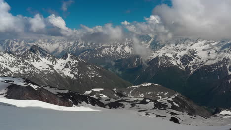 Air-flight-through-mountain-clouds-over-beautiful-snow-capped-peaks-of-mountains-and-glaciers.