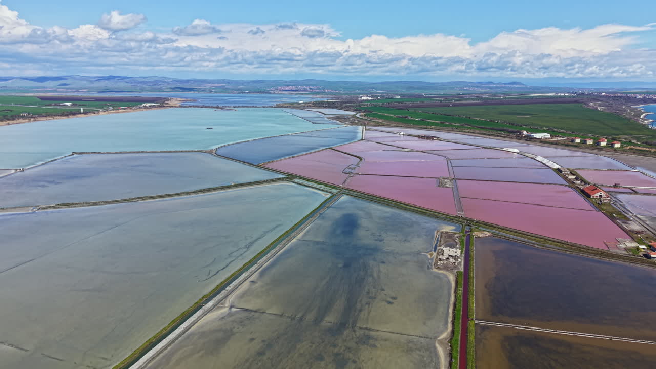 Saltflater er synlige på et luftfoto av landskapet, som viser ulike farger og mønstre på vann og land på dagtid nær et kystområde.