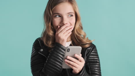 adolescente caucásica con chaqueta de cuero usando su teléfono inteligente y sonriendo.