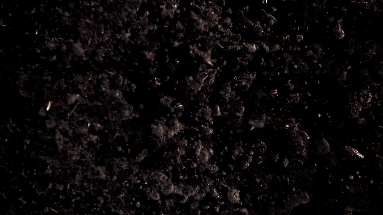Particelle di terra scura che cadono e galleggiano su uno sfondo nero.