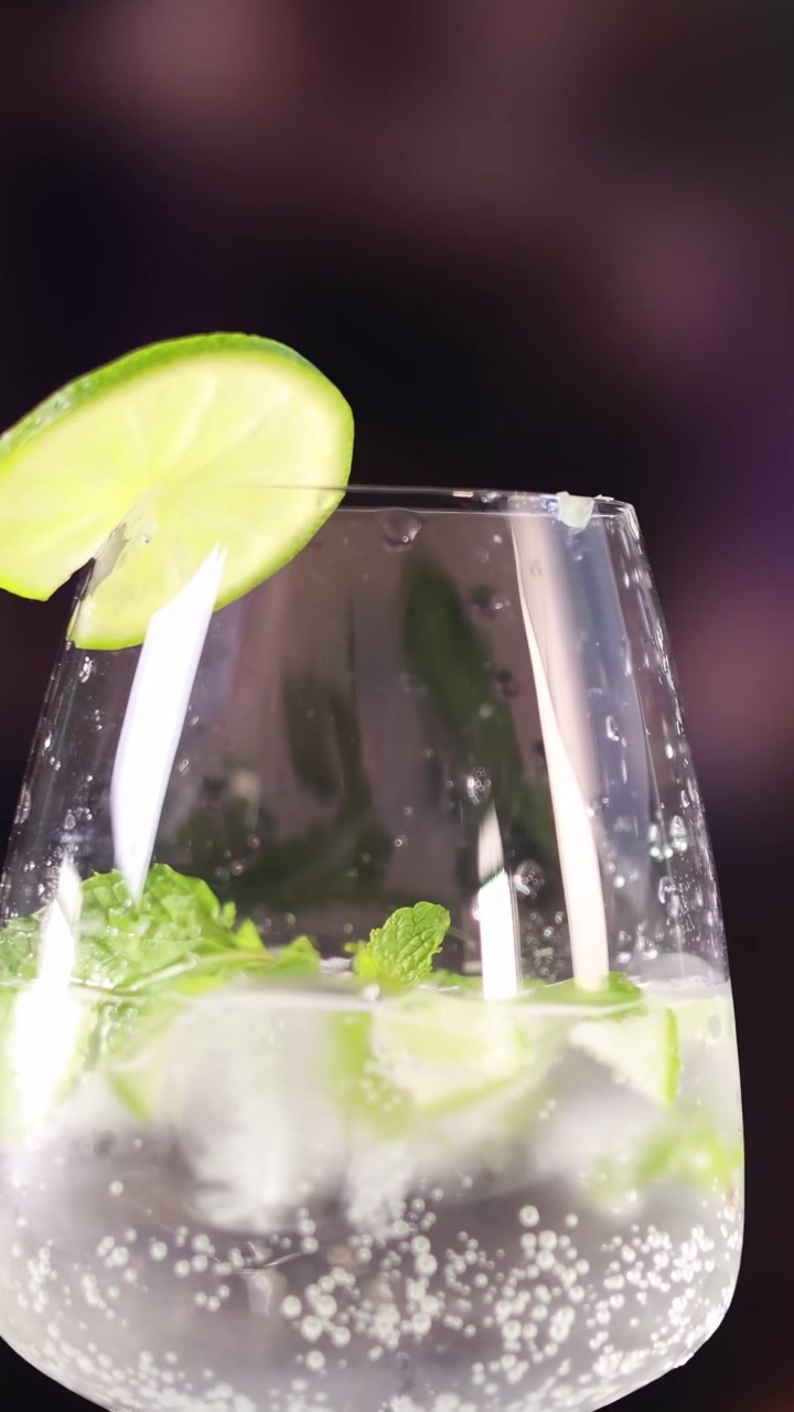 Un cocktail mojito con lime e menta in un bicchiere trasparente su uno sfondo sfocato e colorato.
