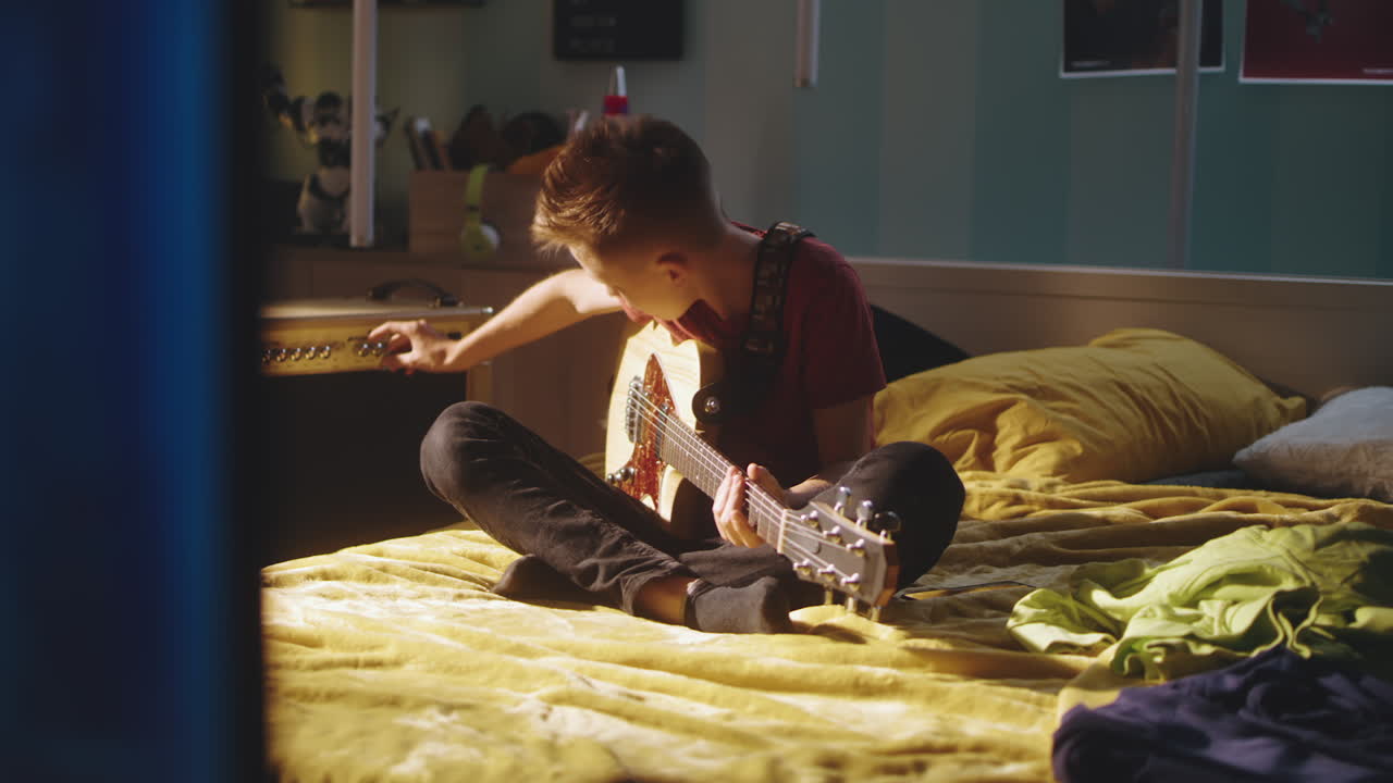 Teenage Boy Playing around with Chord Changes on Acoustic Guitar at Home Caucasian Teenage Boy with Curly Hair Playing around with Chord Changes on Acoustic Guitar while Spending Free Time at Home