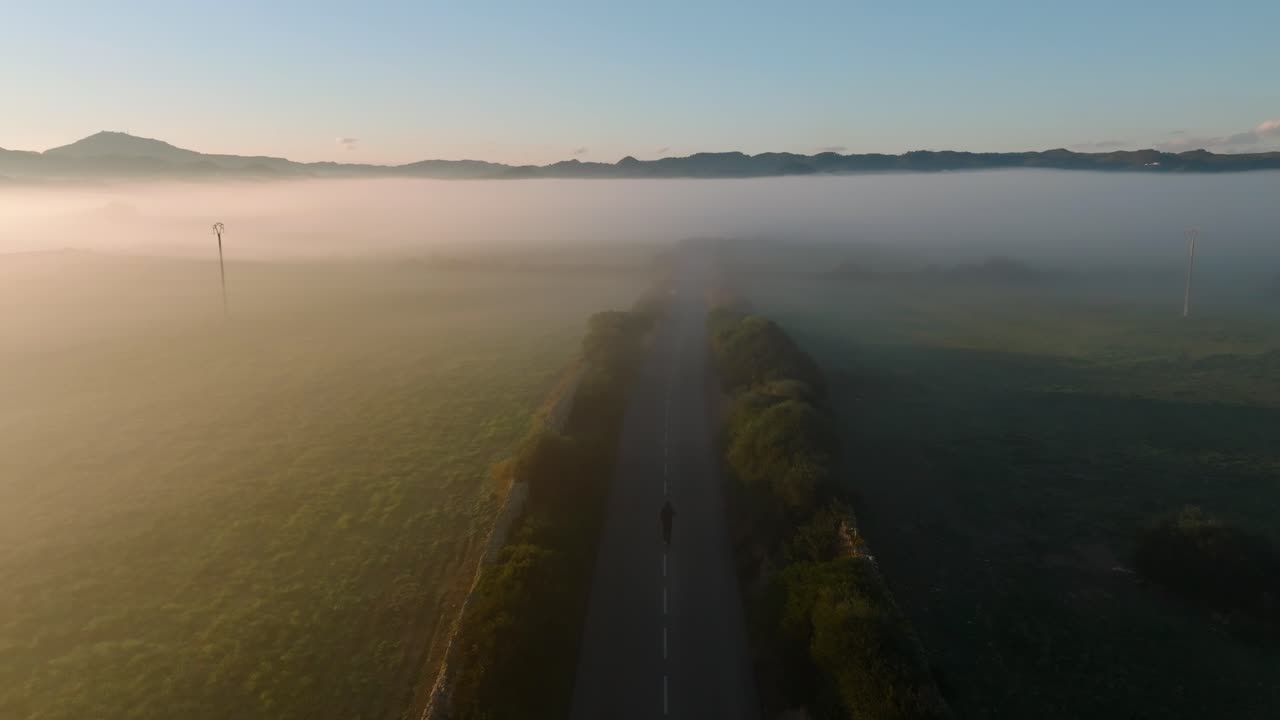 Road between foggy mountain valley with a person morning jogging aerial drone panoramic view