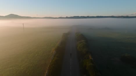 Straße-Zwischen-Nebligem-Bergtal-Mit-Einer-Person,-Die-Morgens-Joggt,-Luftdrohne-Mit-Panoramablick