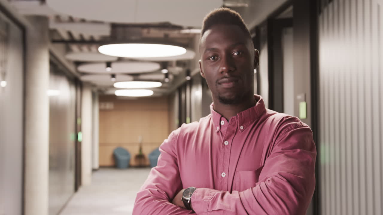 Confident businessman standing with arms crossed in modern office hallway