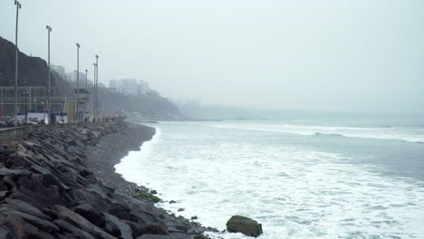 Static-shot-of-a-foggy-morning-off-the-coast-of-Roquitas,-Malecon-de-Miraflores,-Lima,-Peru-with-waves-at-a-rocky-beach