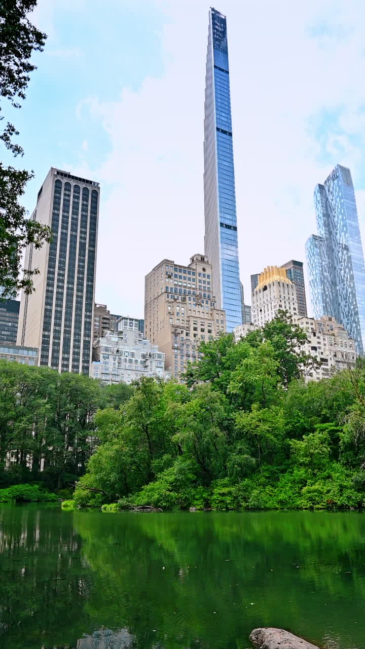 Discovering Central Park's greens. Visitors admire serene views of lush trees and buildings reflecting on water in Central Park, Manhattan