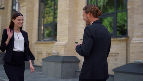 Man-using-mobile-phone-while-going-to-work.-Colleagues-greeting-each-other.