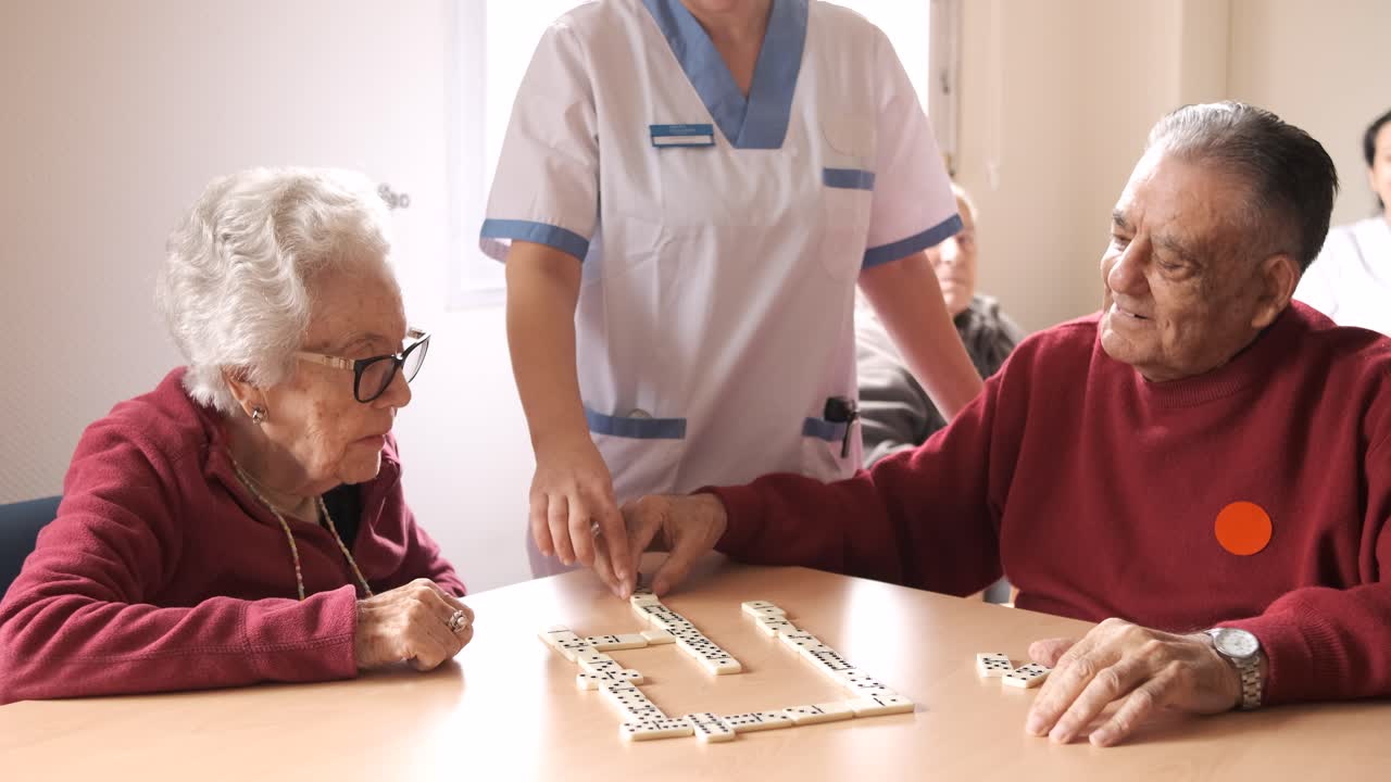 Nurse playing dominoes with senior man and woman in canteen of nursing home