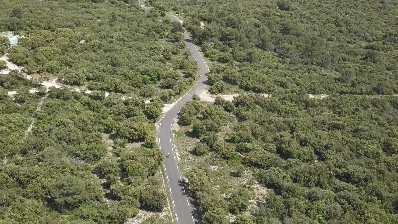 An aerial view of a cyclist passing next to an oncoming vehicle and continuing the cycle.