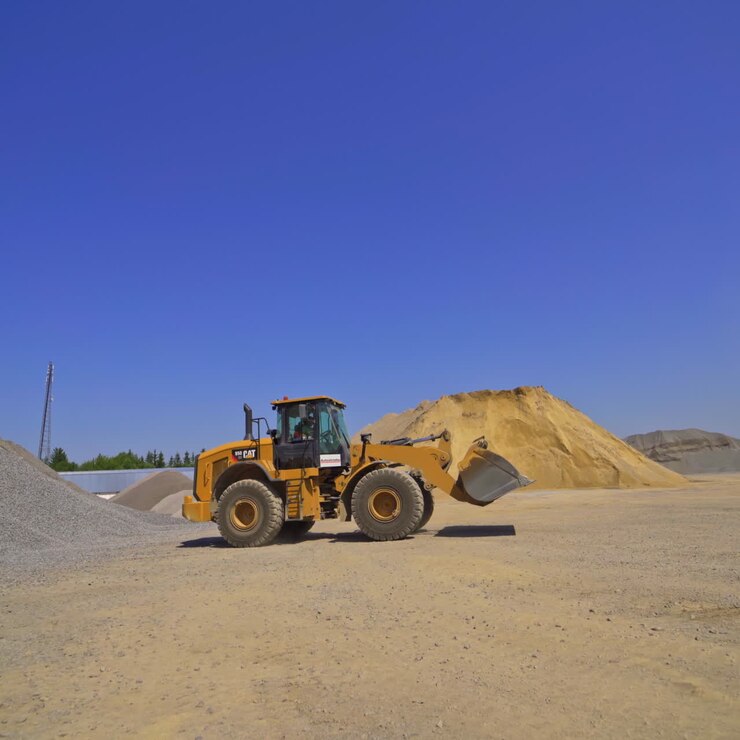 Excavator moving among piles of gravel. Asphalt plant. Industrial machinery working outdoors.