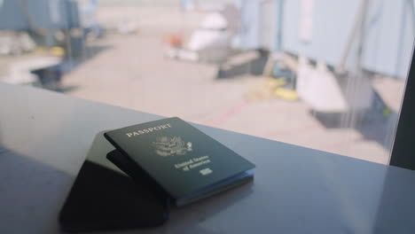 hands holding passport and smartphone while waiting to board flight in airport terminal or gate