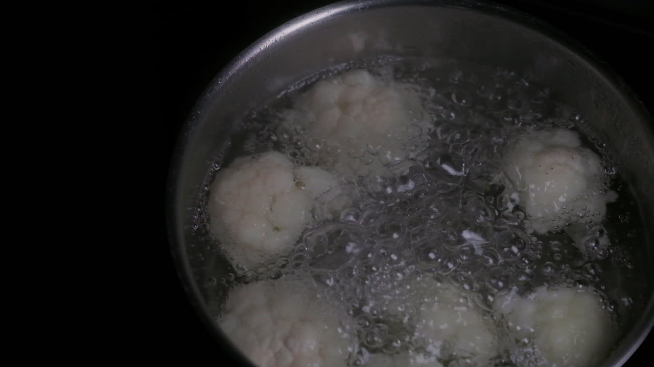 Blomkål koker og bobler i en panne med vann på en kokeplate