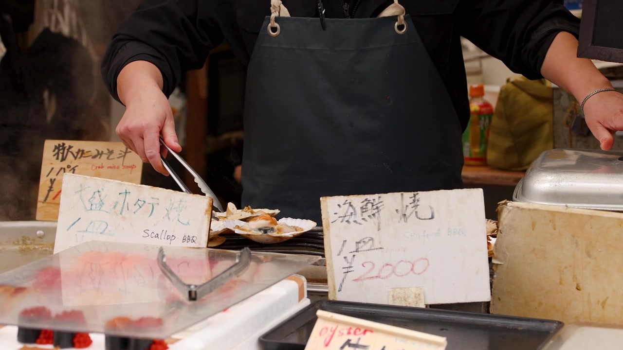 A chef uses tongs to grill fresh scallops at Tsukiji Market in Tokyo, Japan.