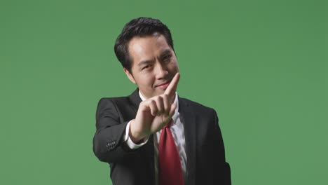 아시아 사업가 한 명이 스, 한 손가락 제스처, 금기 표지판을 보여주며 스튜디오의 녹색 스크린에 서 있습니다.