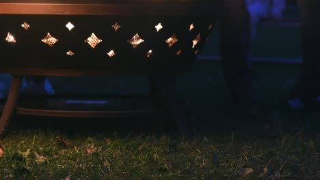 Low-angle-view-of-a-fire-pit-at-a-camp-fire,-with-people-walking-around-it