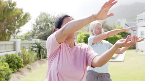 Dos-Mujeres-Mayores-Diversas-Y-Enfocadas-Practicando-Yoga-En-Un-Jardín-Soleado,-Cámara-Lenta,-Espacio-Para-Copiar