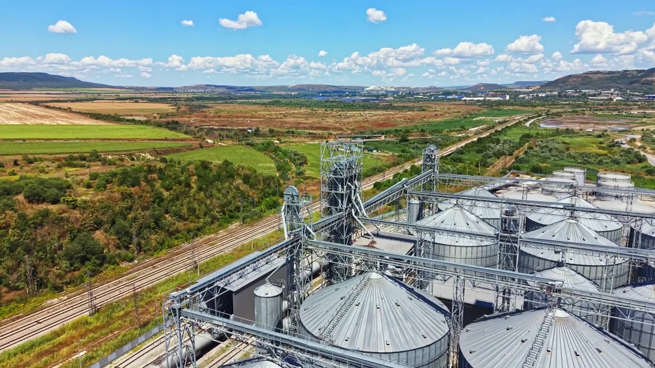 View of silos and train tracks near fields in a rural area under a blue sky with clouds during daytime