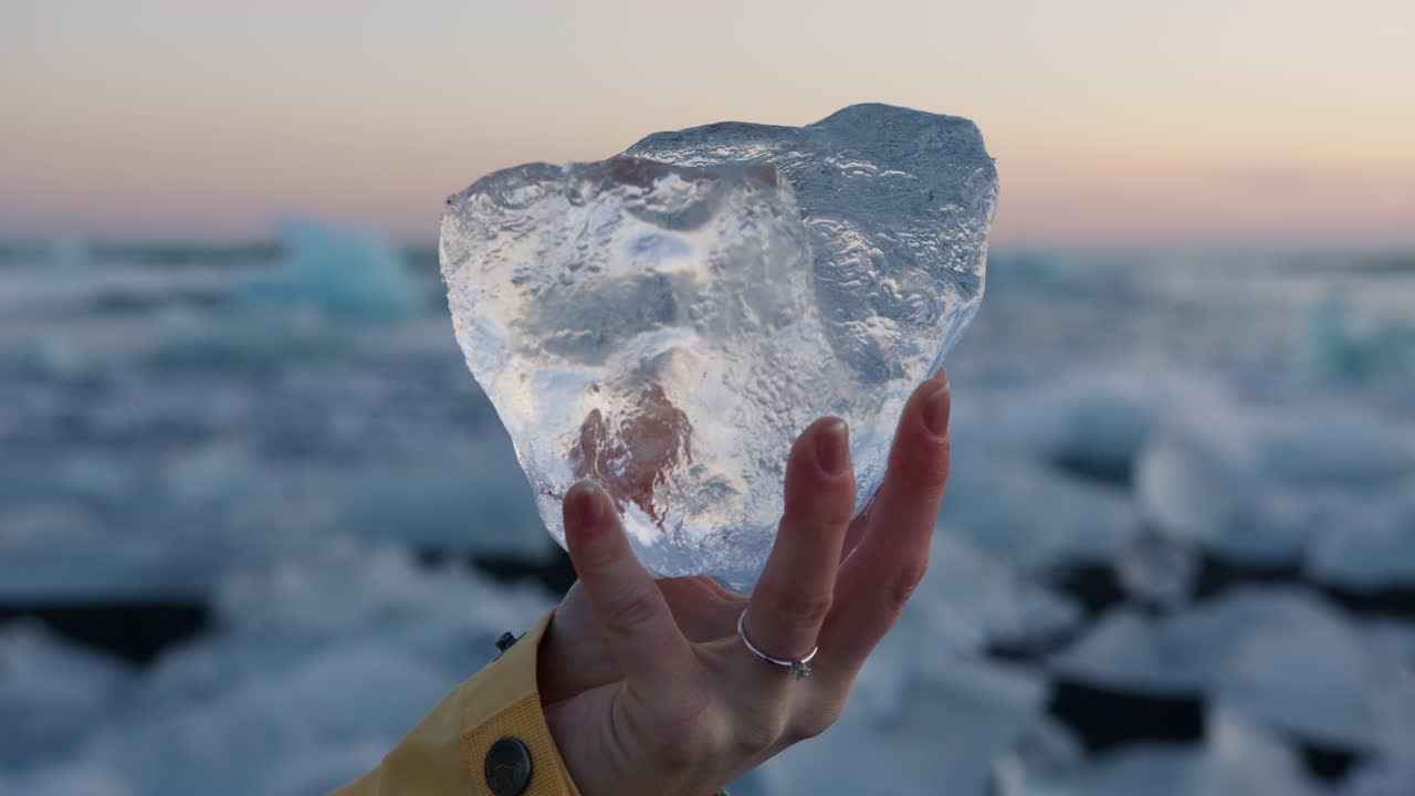 mujer sosteniendo un gran bloque de hielo en la playa de diamantes en islandia