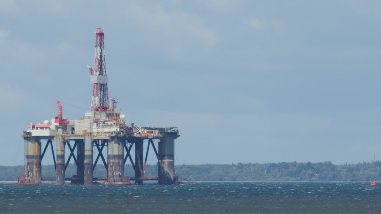 Large offshore oil drilling platform stands in choppy sea near Cromarty, Scotland. Daylight, wide shot, steady camera, overcast sky, industrial maritime setting