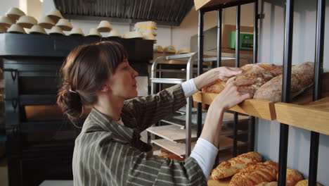 Woman-Putting-Fresh-Bread-on-Display-Rack-in-Bakery