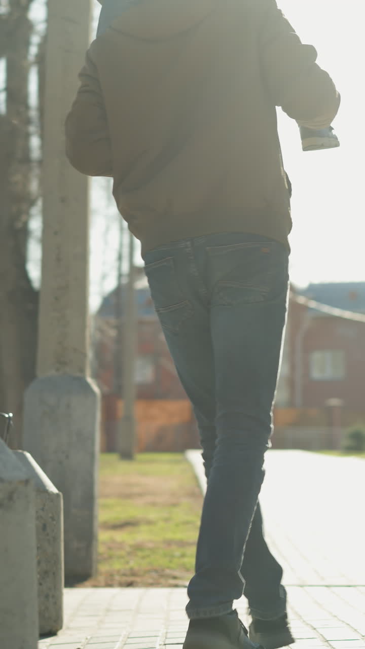 un padre corre juguetón alrededor de una barrera de hormigón mientras lleva a su hijo en los hombros, el padre sostiene cuidadosamente las piernas del niño para mantener el equilibrio, ambos vestidos con chaquetas