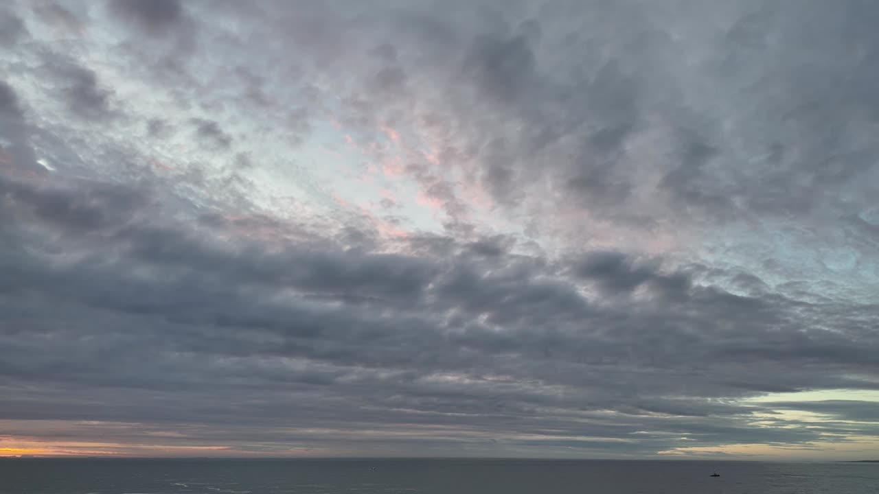 Time lapse of textured clouds moving over the ocean during the transition to sunset.