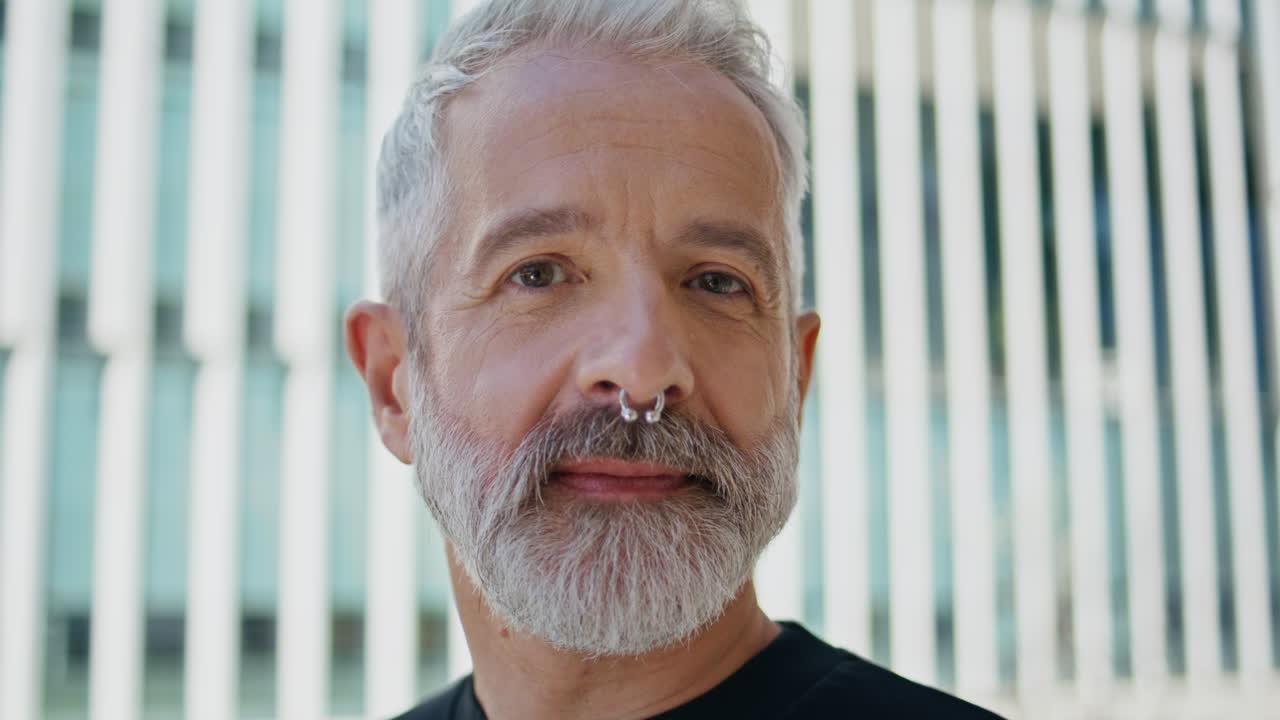 hombre de cabello gris posando en un edificio urbano en primer plano. un anciano brutal con un anillo en la nariz.