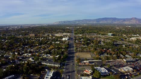 Dolly-in-tilt-up-aerial-drone-extreme-wide-landscape-shot-of-the-Salt-Lake-county-valley-covered-in-buildings,-busy-roads,-and-colorful-autumn-trees-on-a-warm-sunny-fall-evening-in-Utah