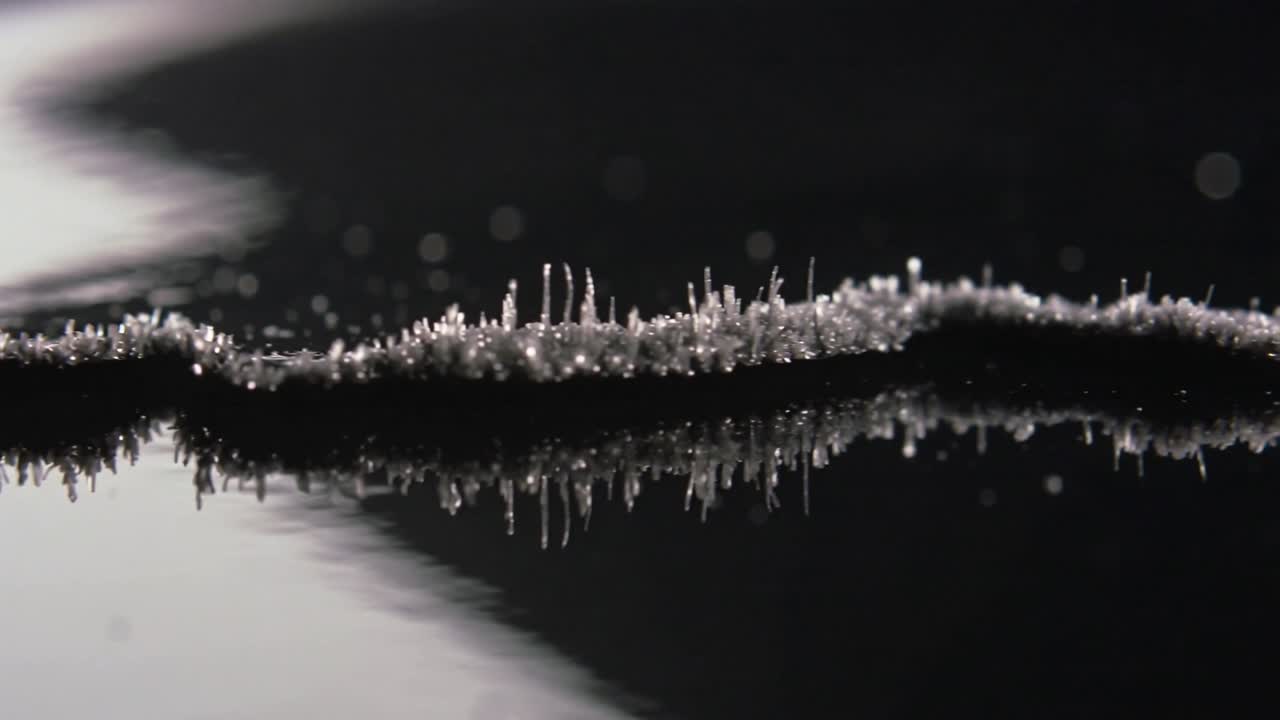 Formazione di cristalli su filamento metallico, luce dall'alto a sinistra che causa punte verticali in studio su specchio scuro