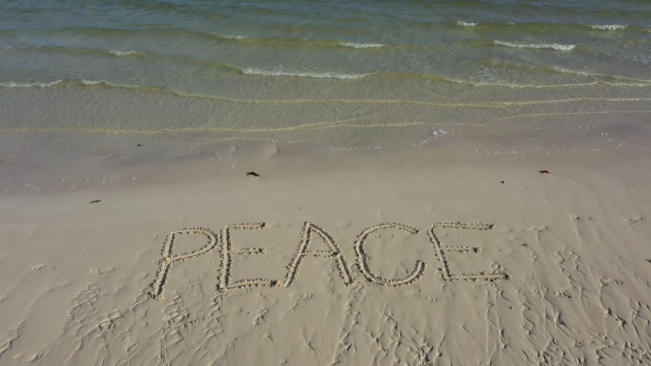 PEACE inscribed in the sand on a beach with water lapping up on the beach